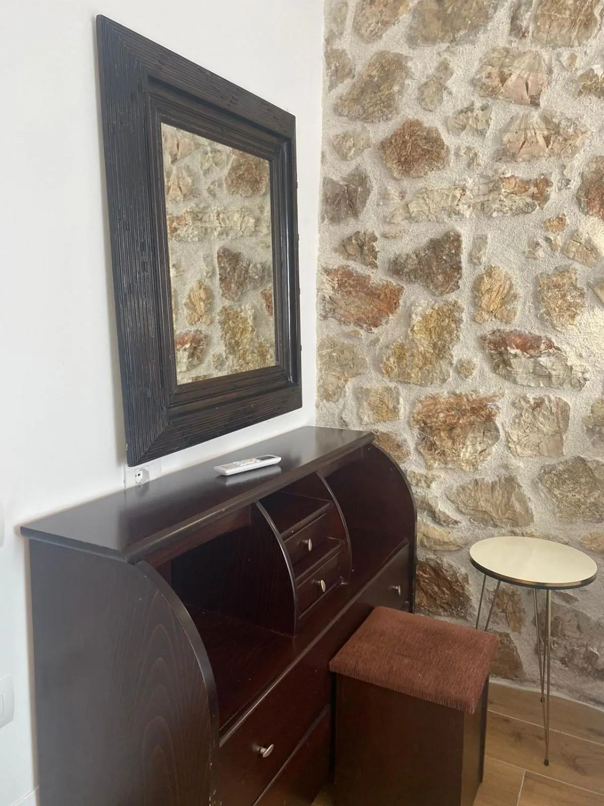 A dark writing bureau and stool under a mirror on the stone wall