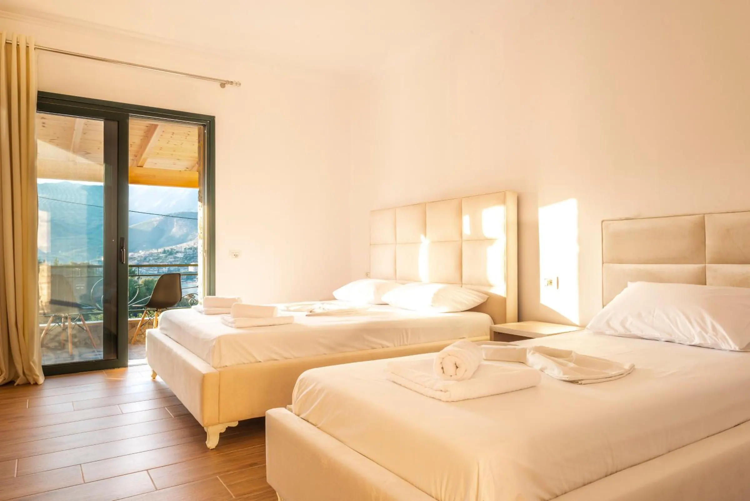 A large double and a single bed with padded white headboards, and a glass door open onto the balcony and the bay