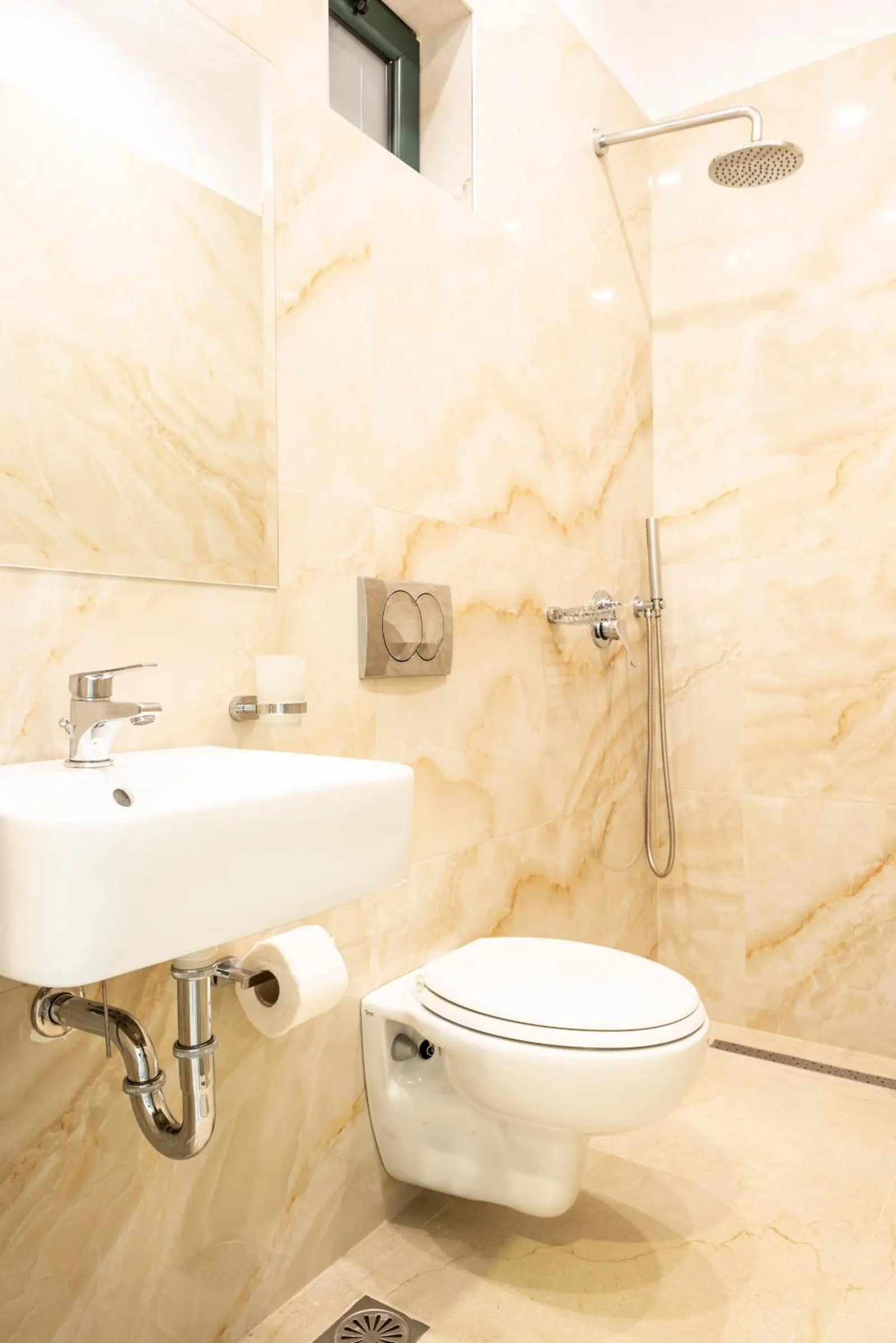 A shower room in cream marble-effect tile with a rain shower, a basin and a wall-hung toilet