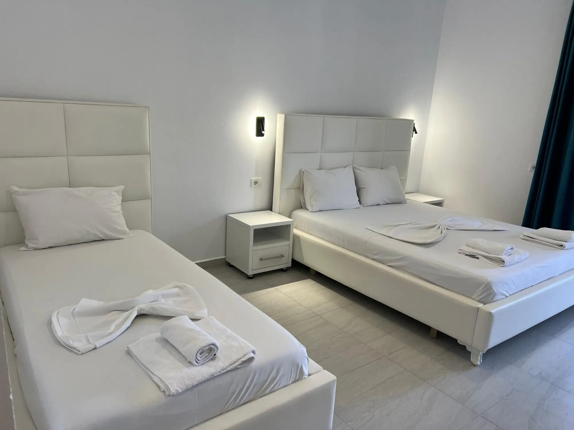 A single and a double bed with tall white headboards and white bedside tables