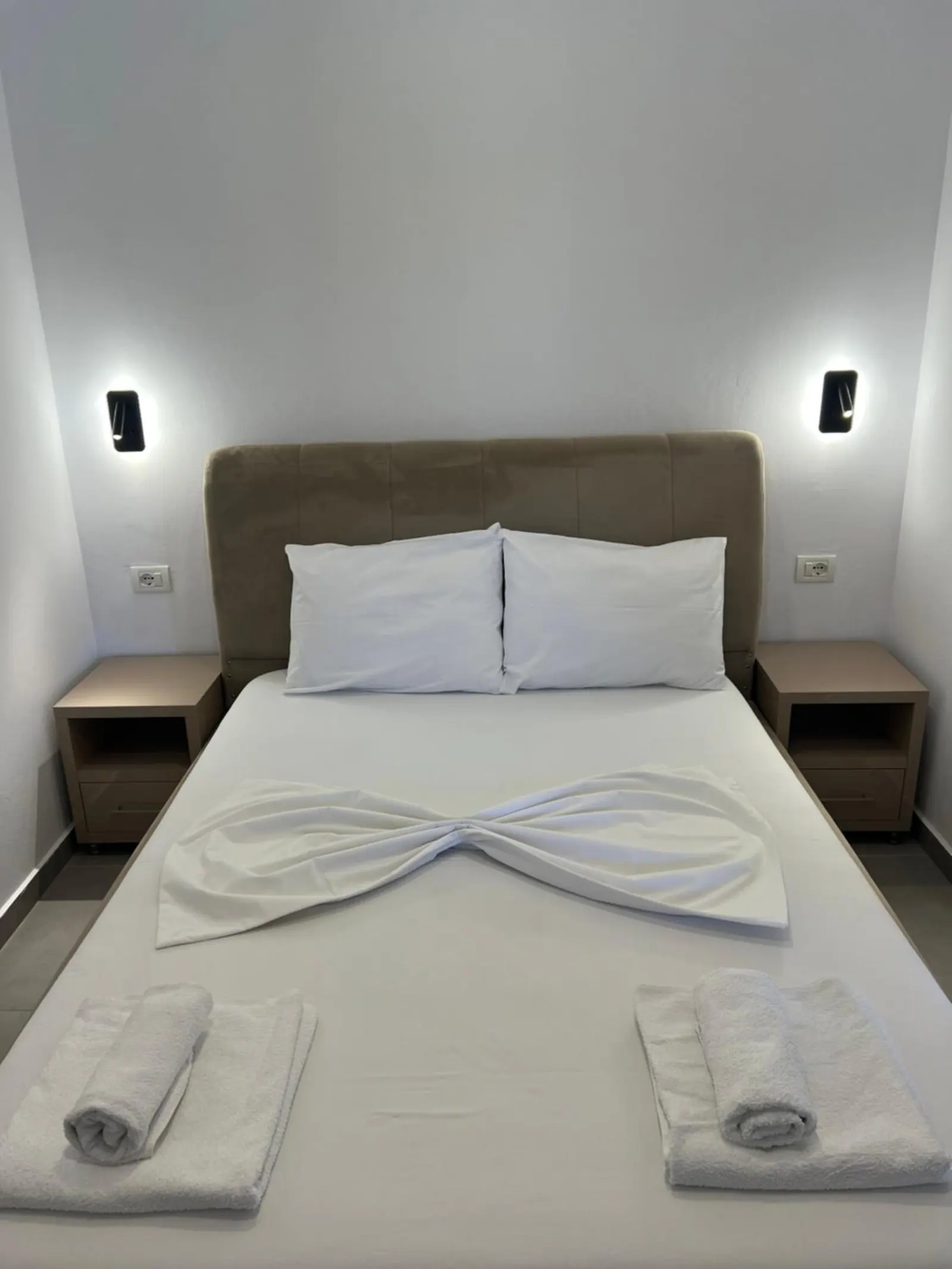 A double bed with a greige upholstered headboard and wall lights either side