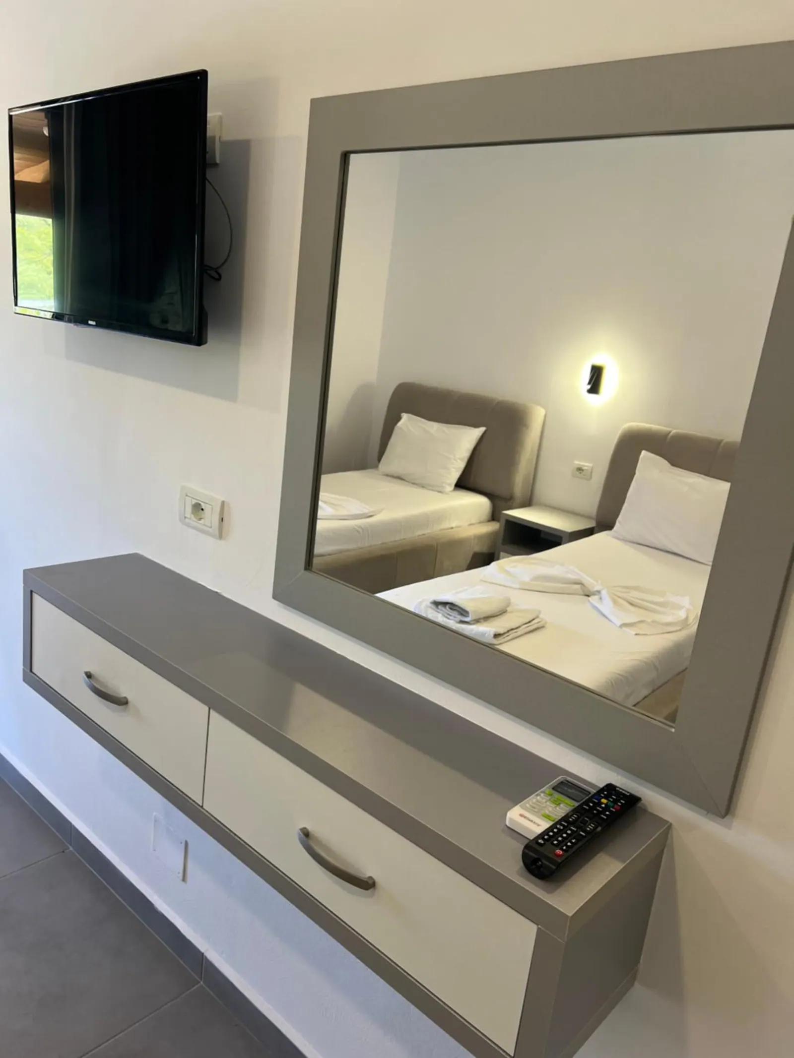 A grey dresser and a large mirror, a television on the wall above