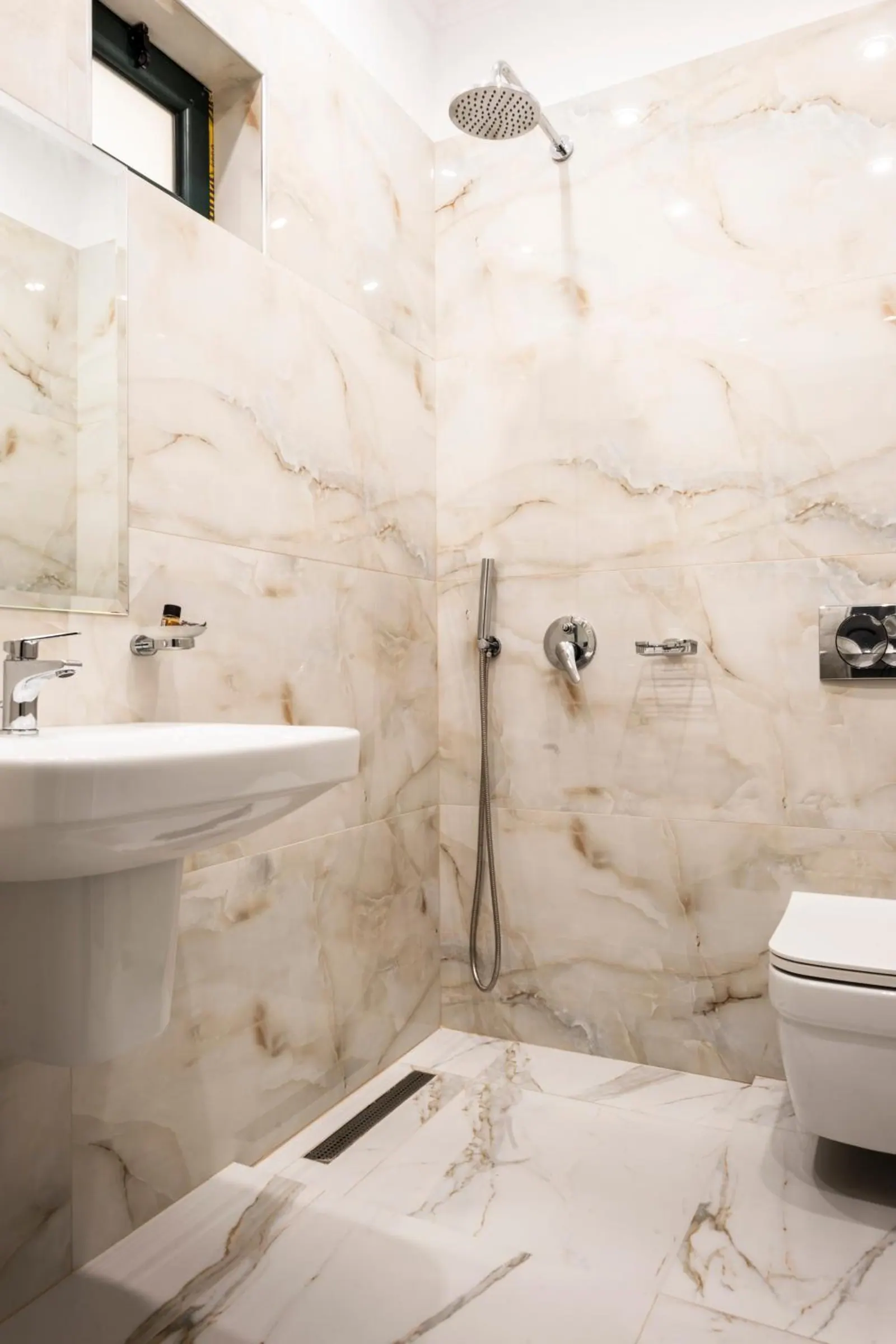 A shower room in white marble-effect tile with a rain shower and a wall-hung toilet