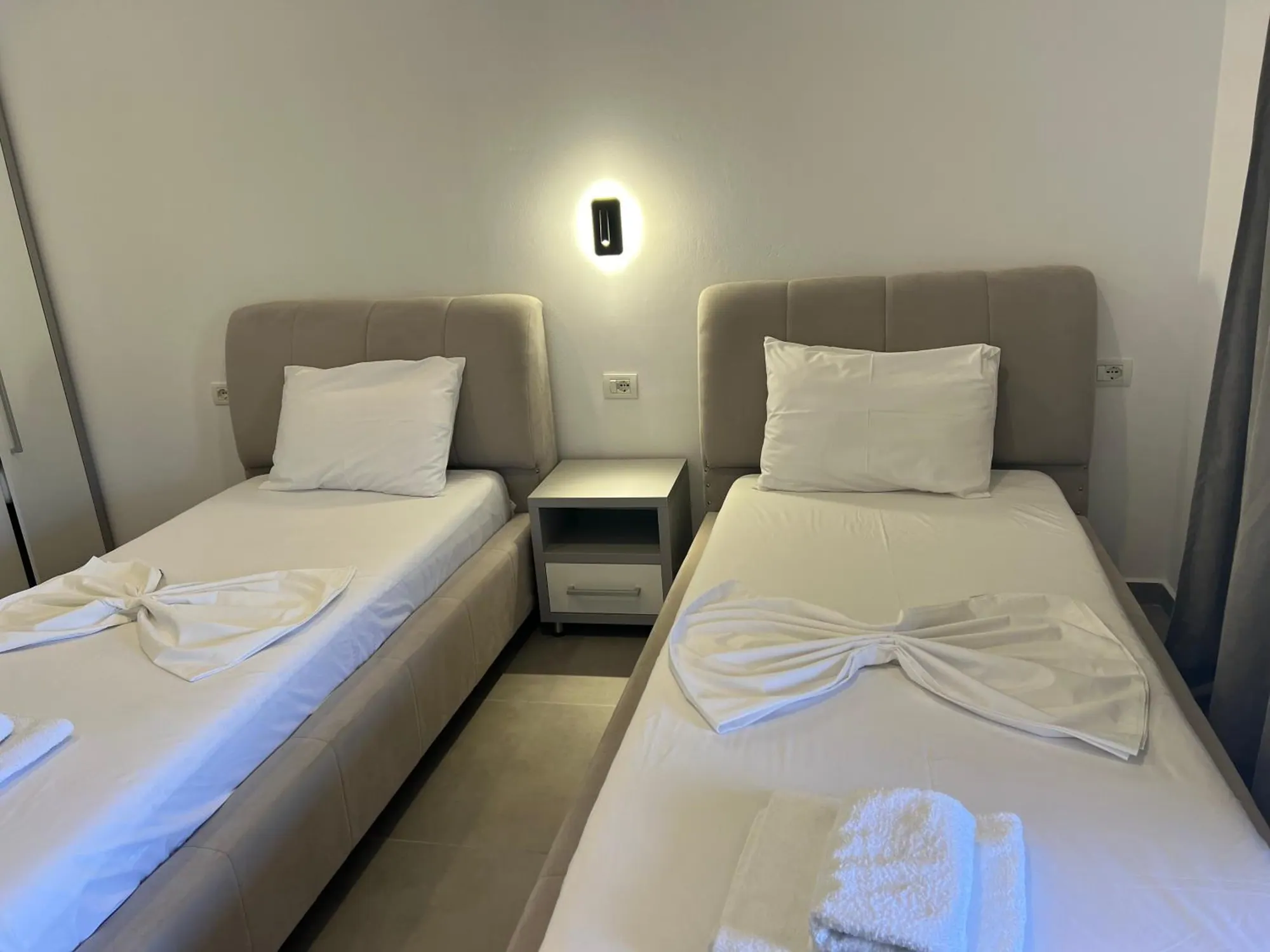 Two single beds with greige upholstered headboards and a white bedside table between them