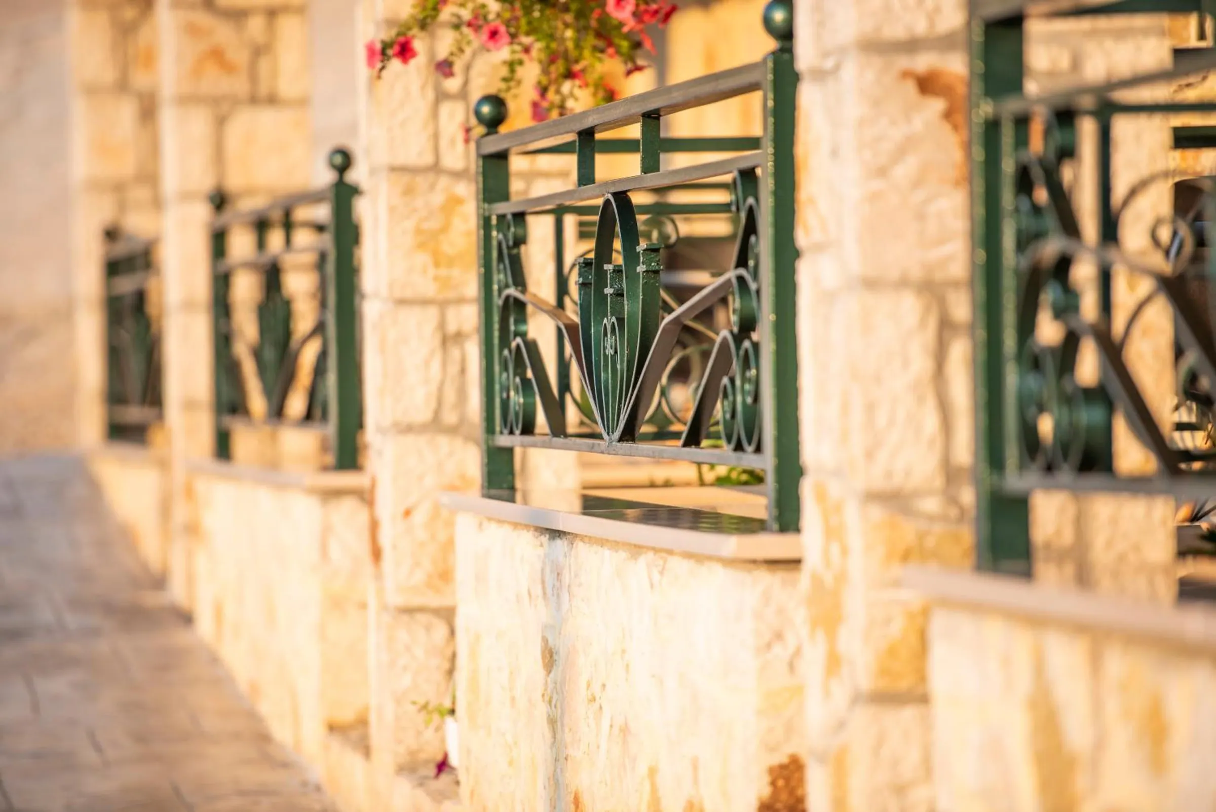 A row of green wrought-iron balcony rails between stone pillars, with flowers trailing over the nearest one