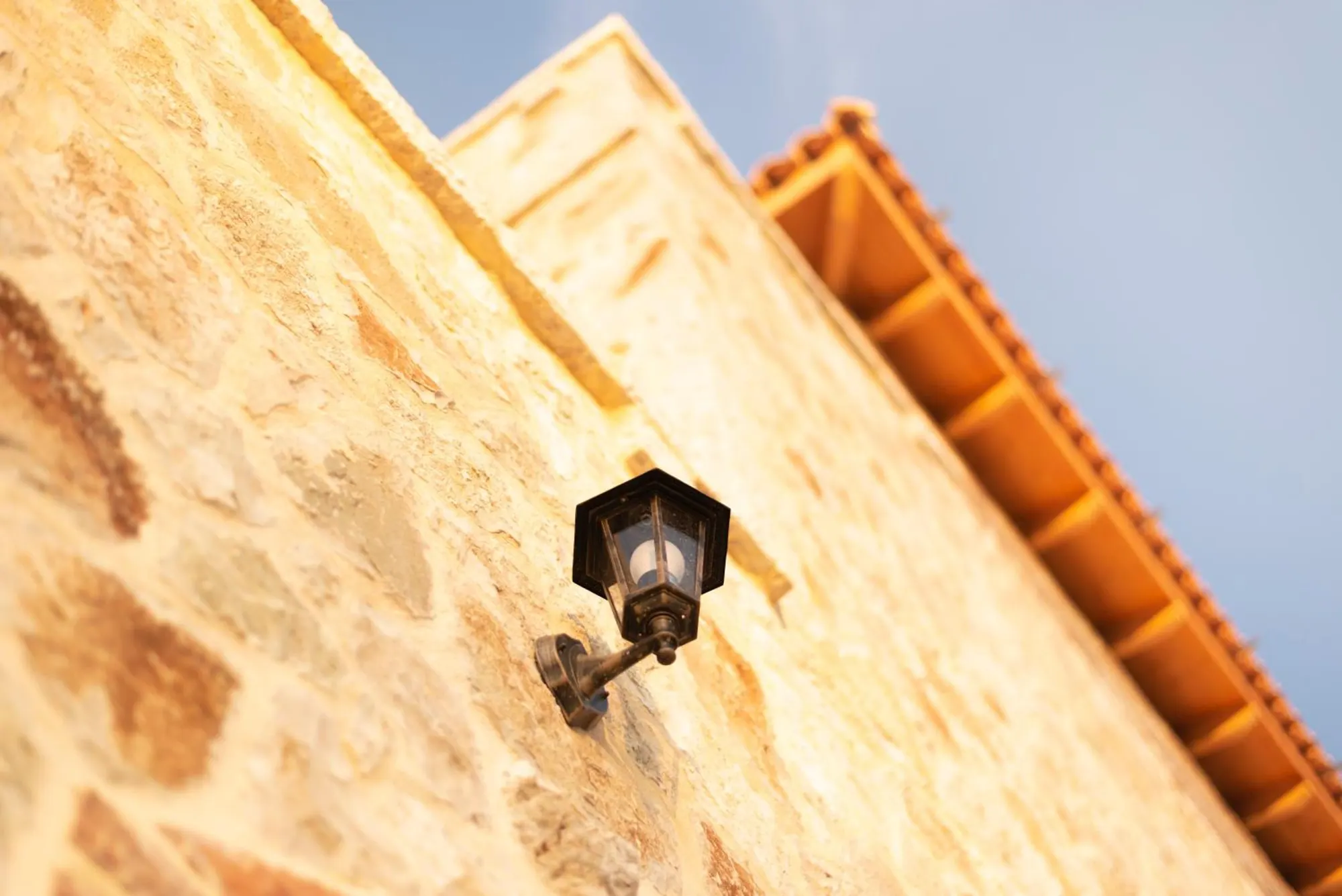 A black lantern on the stone wall under the terracotta eaves