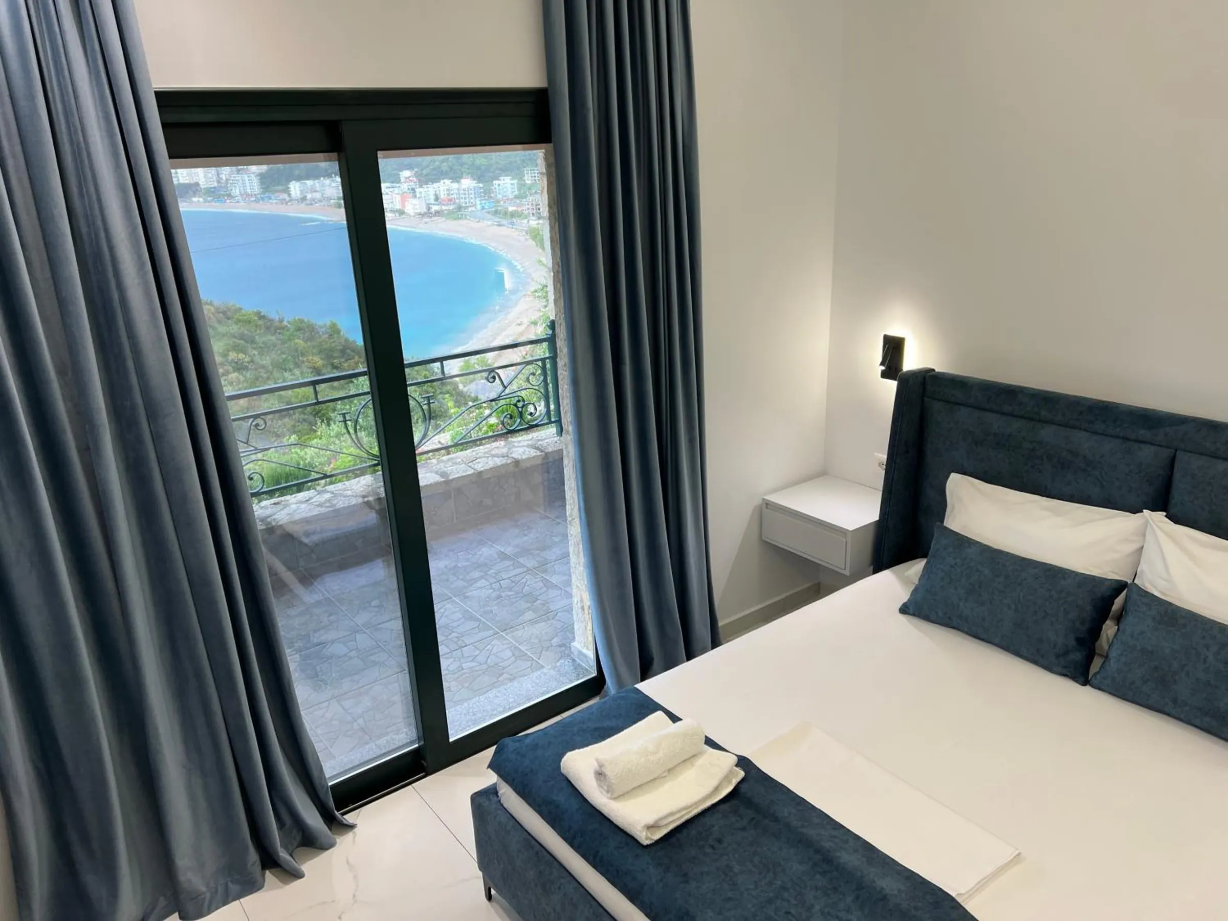 From the bed, the glass door and navy curtains framing the curve of Potam bay