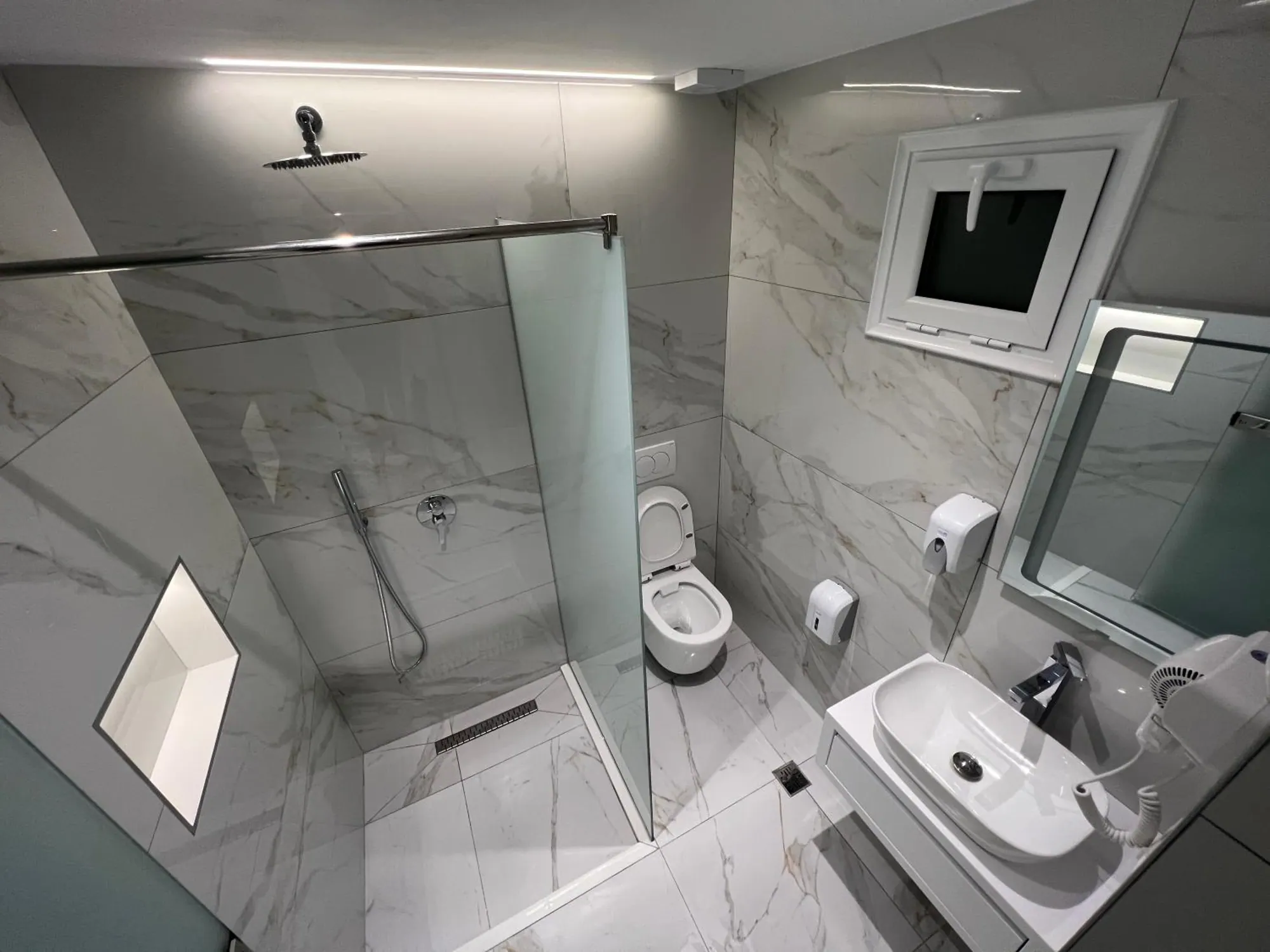 A grey marble shower room with a glass screen, a vessel basin and a lit mirror