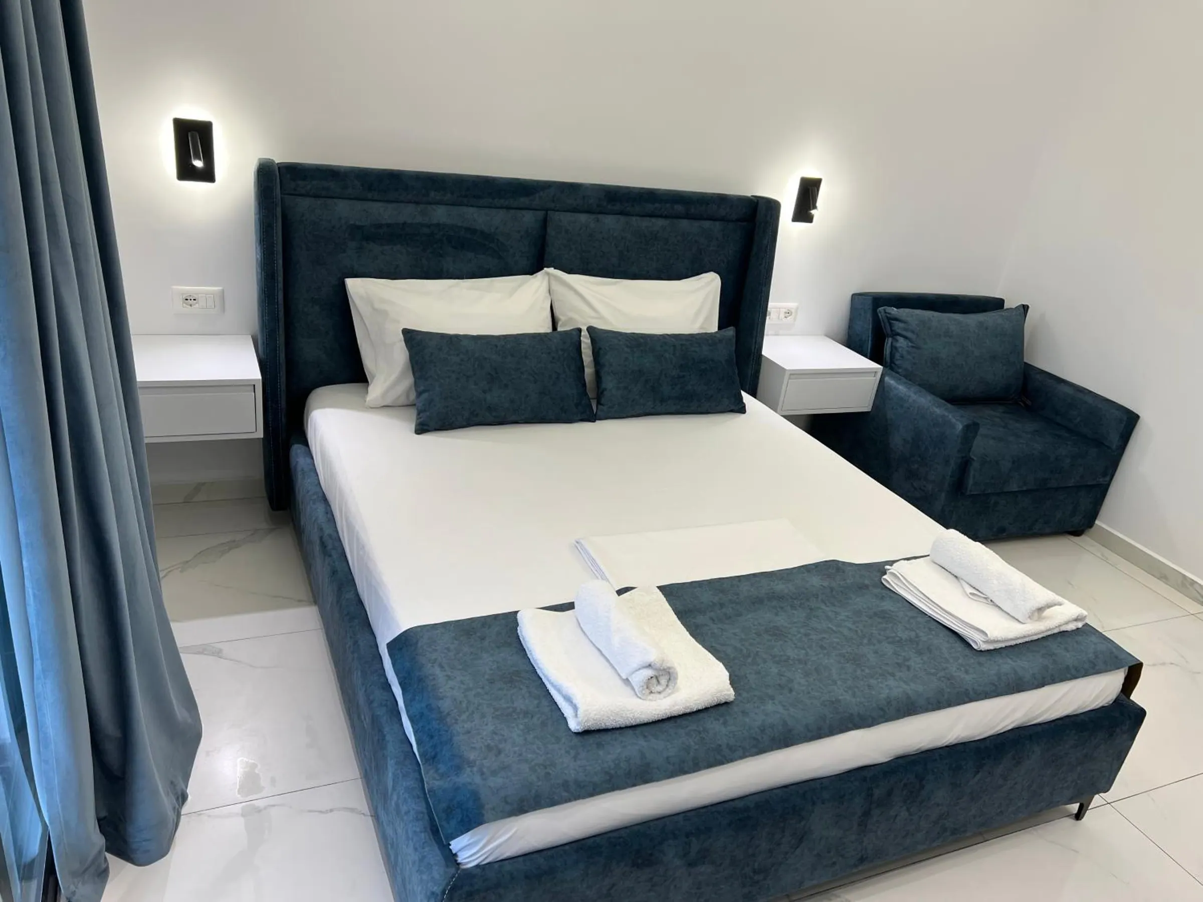 The navy velvet bed with cushions and folded towels, a velvet armchair beside it