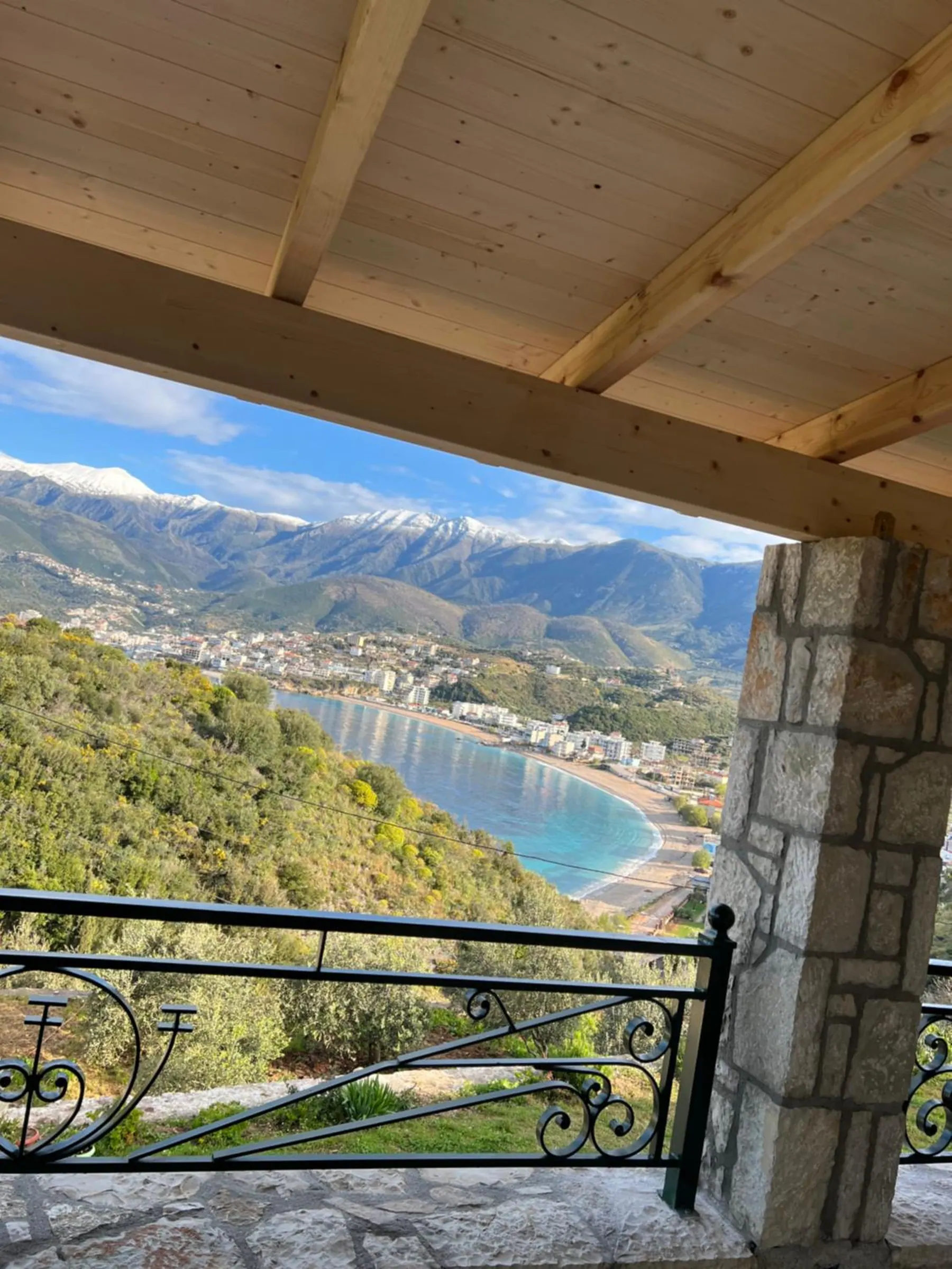 Looking out from under the timber roof past a stone pillar, the bay below and snow on the mountains behind the town