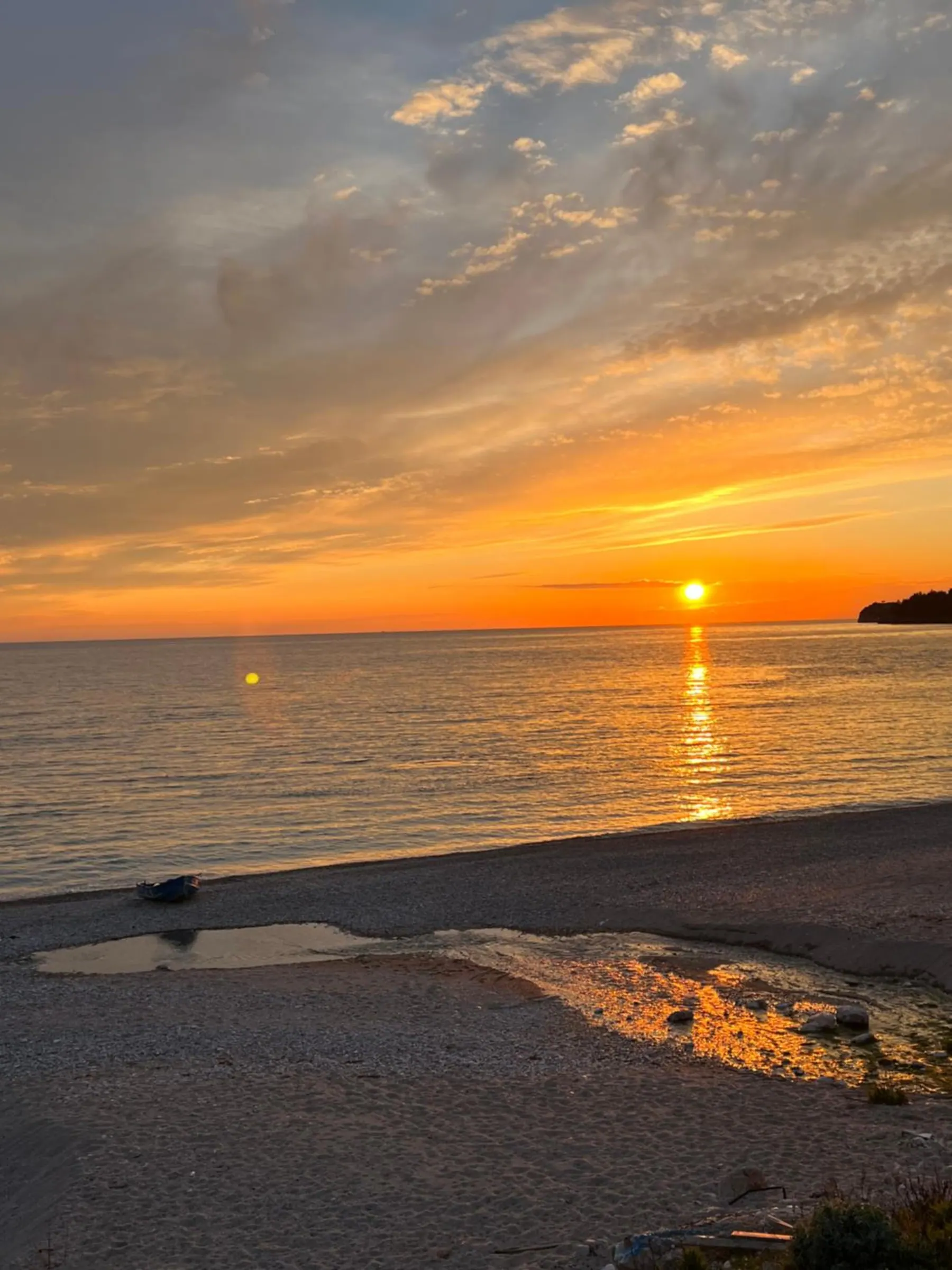 The sun going down over the sea from a beach of sand and shingle