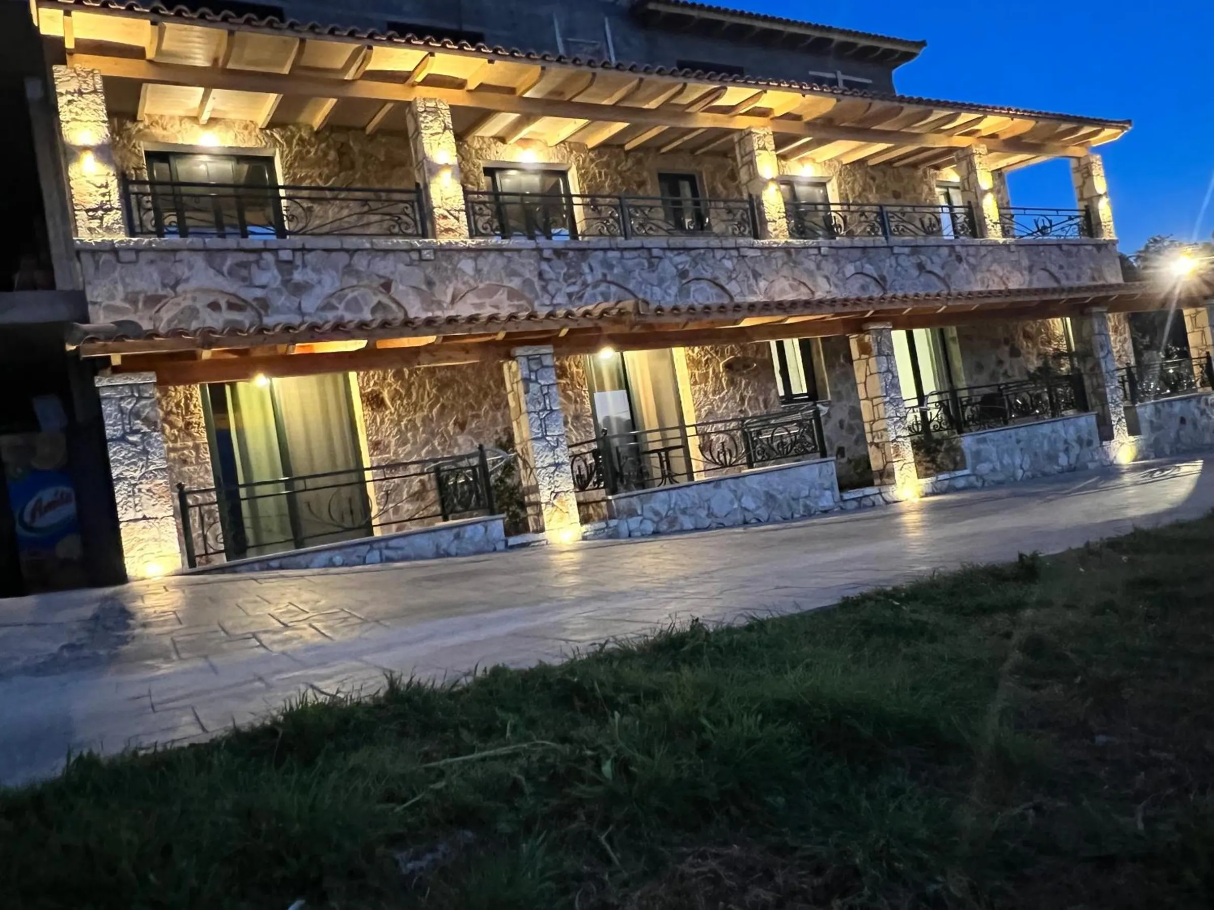 Stonevilla Buta at dusk, two floors of stone and timber lit from below, wrought-iron balconies along both floors and the lawn in front