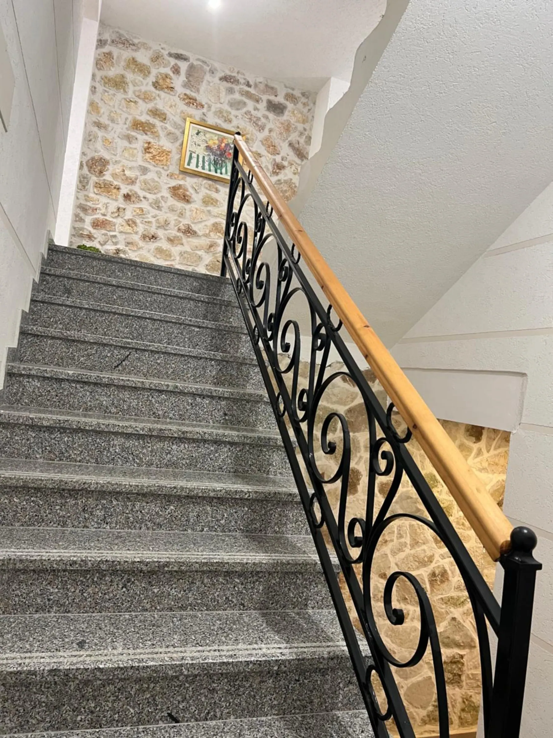Granite stairs with a wrought-iron banister and a timber handrail, climbing beside a stone wall