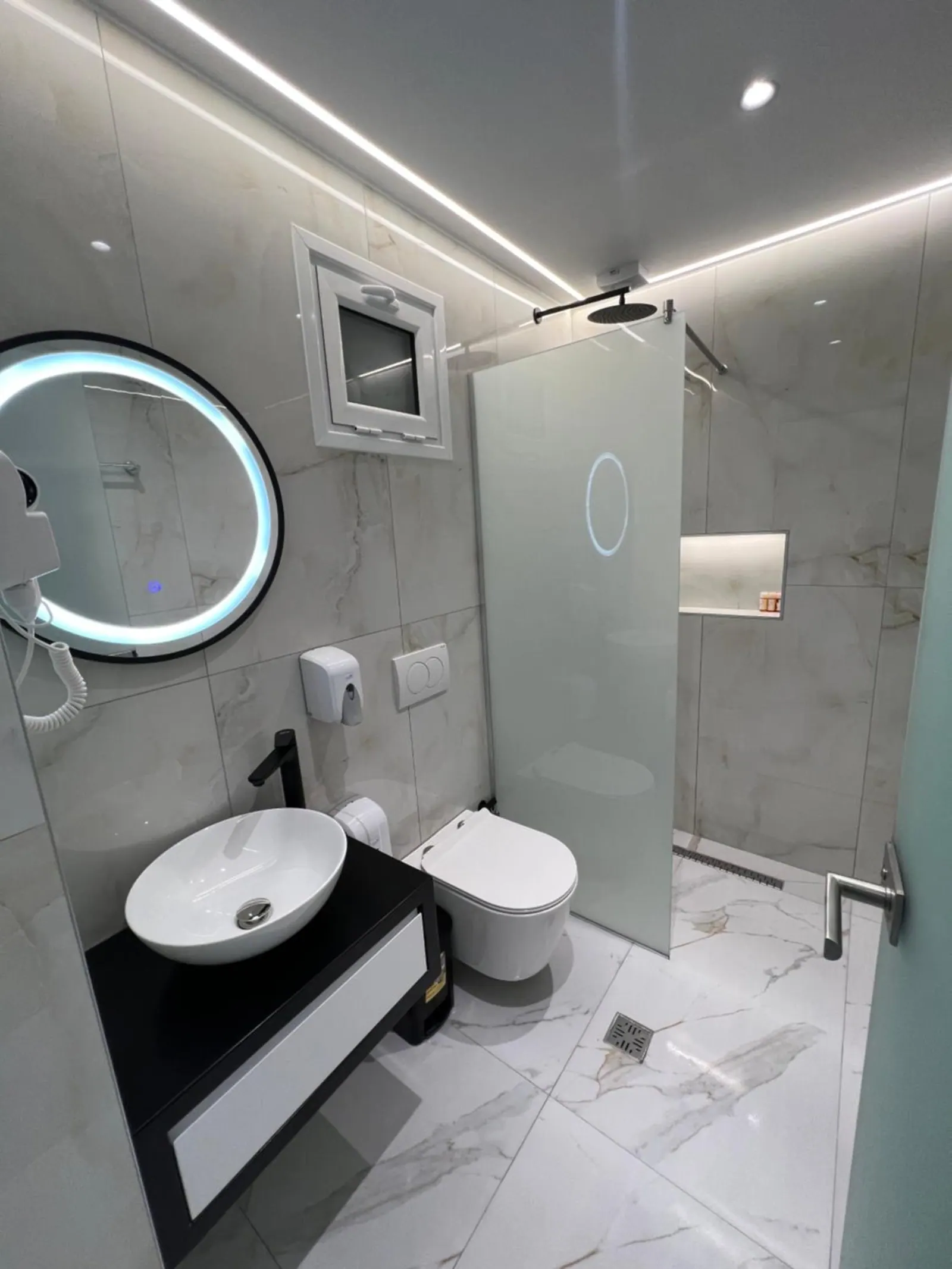 A shower room with a frosted screen, a round lit mirror and a vessel basin on a black stand