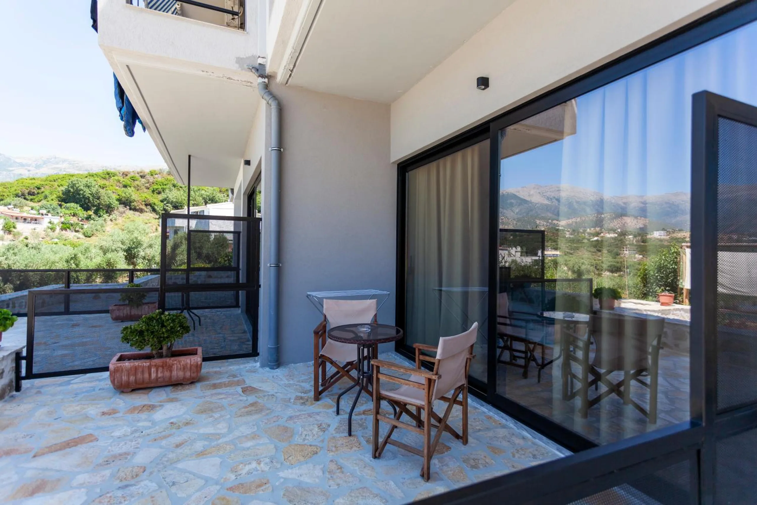 A ground-floor terrace of crazy-paved stone outside sliding glass doors, a small table and two director's chairs, the mountains reflected in the glass