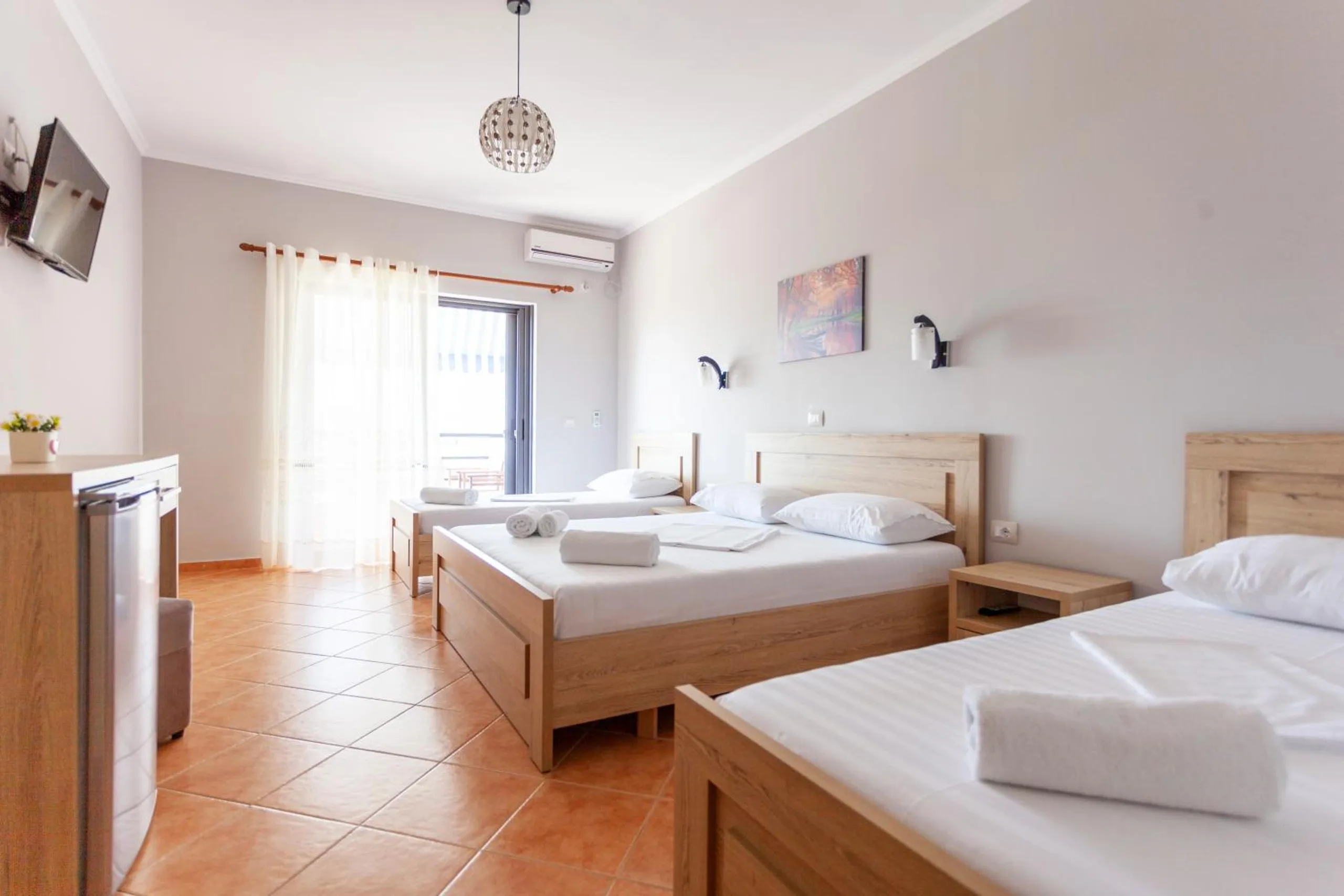 A larger room with a double bed and two singles in pale oak, a desk and fridge on the left, terracotta tiles and a window at the end