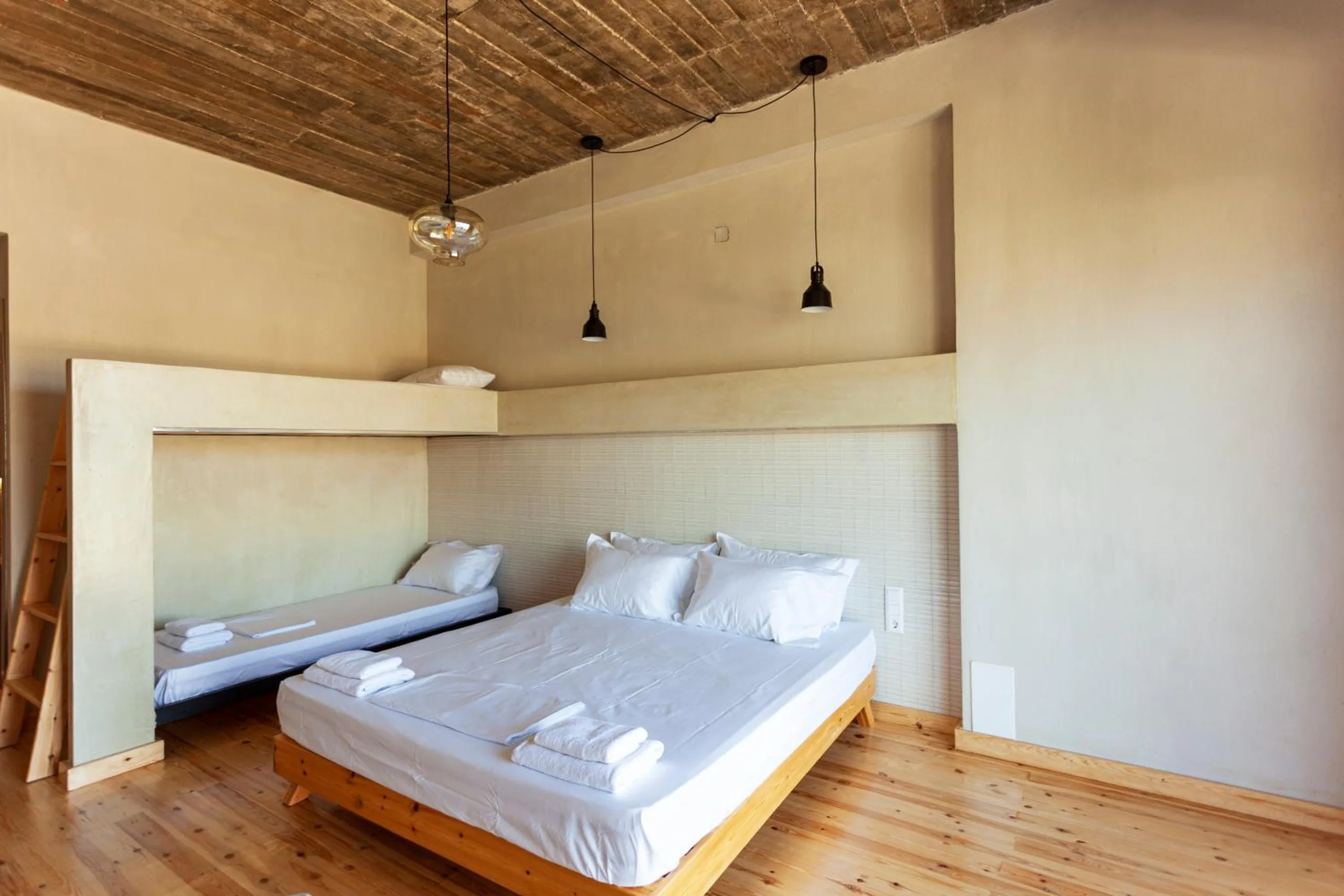 A double bed and a single in a plastered alcove under a timber plank ceiling, with pine floorboards and two black pendant lamps