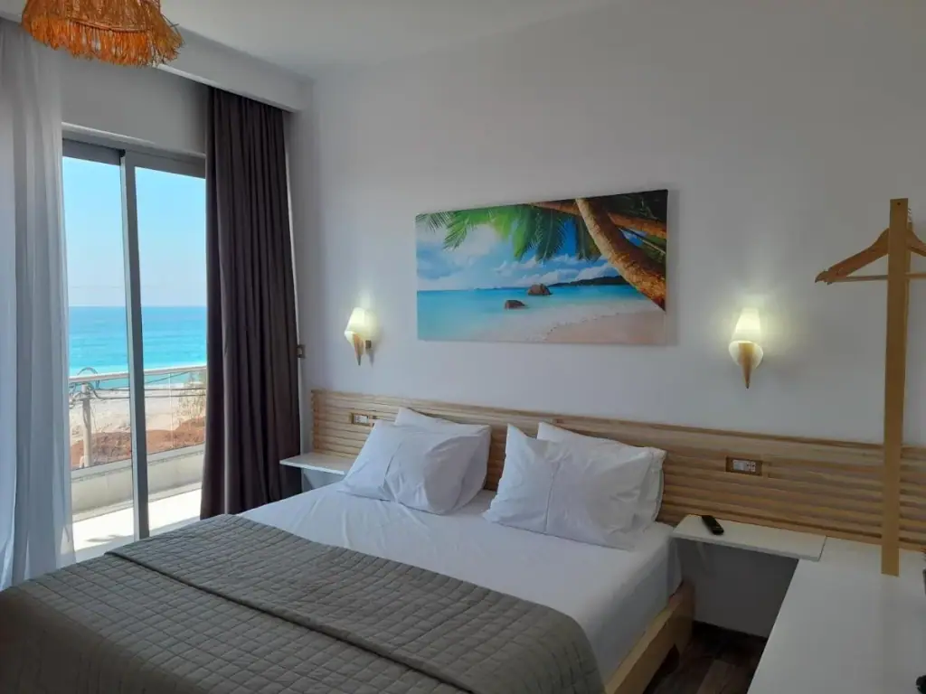 A double bed facing a sliding glass door that opens onto a balcony above Livadhi Beach.