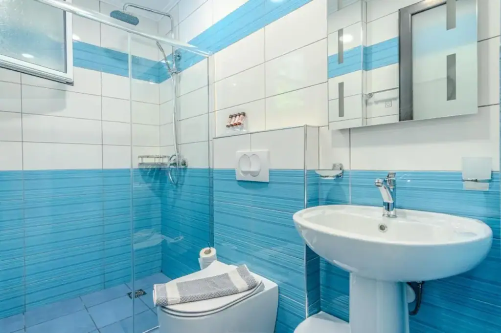A bathroom tiled in blue and white bands with a basin, a mirror and a glazed shower