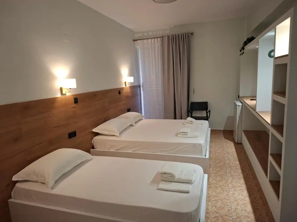 A room at Areti Rooms Hotel with two beds against a full-width oak headboard and two wall lights