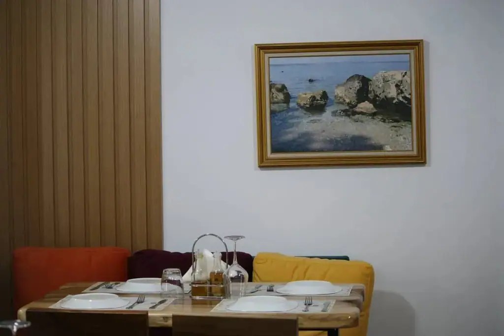 A corner table for three against a timber-slatted wall, with a gold-framed seascape above the banquette