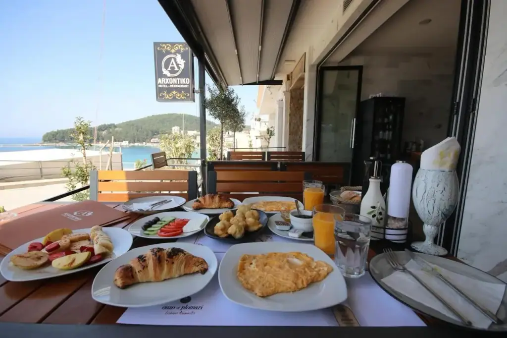 The Arxontiko Hotel-Restaurant sign hanging over a breakfast table on the terrace, with Spile bay behind it