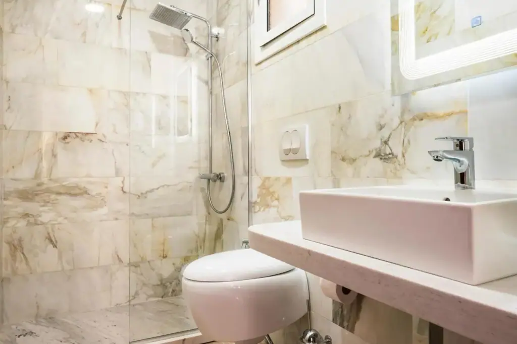 A bathroom clad in honey-veined marble with a walk-in shower and a rectangular vessel basin