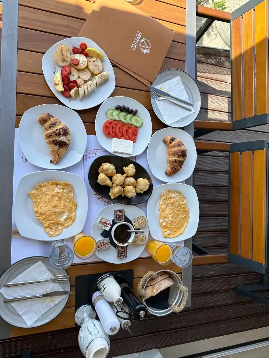 A breakfast spread photographed from above: croissants, omelettes, fried dough balls, tomato, cucumber and white cheese