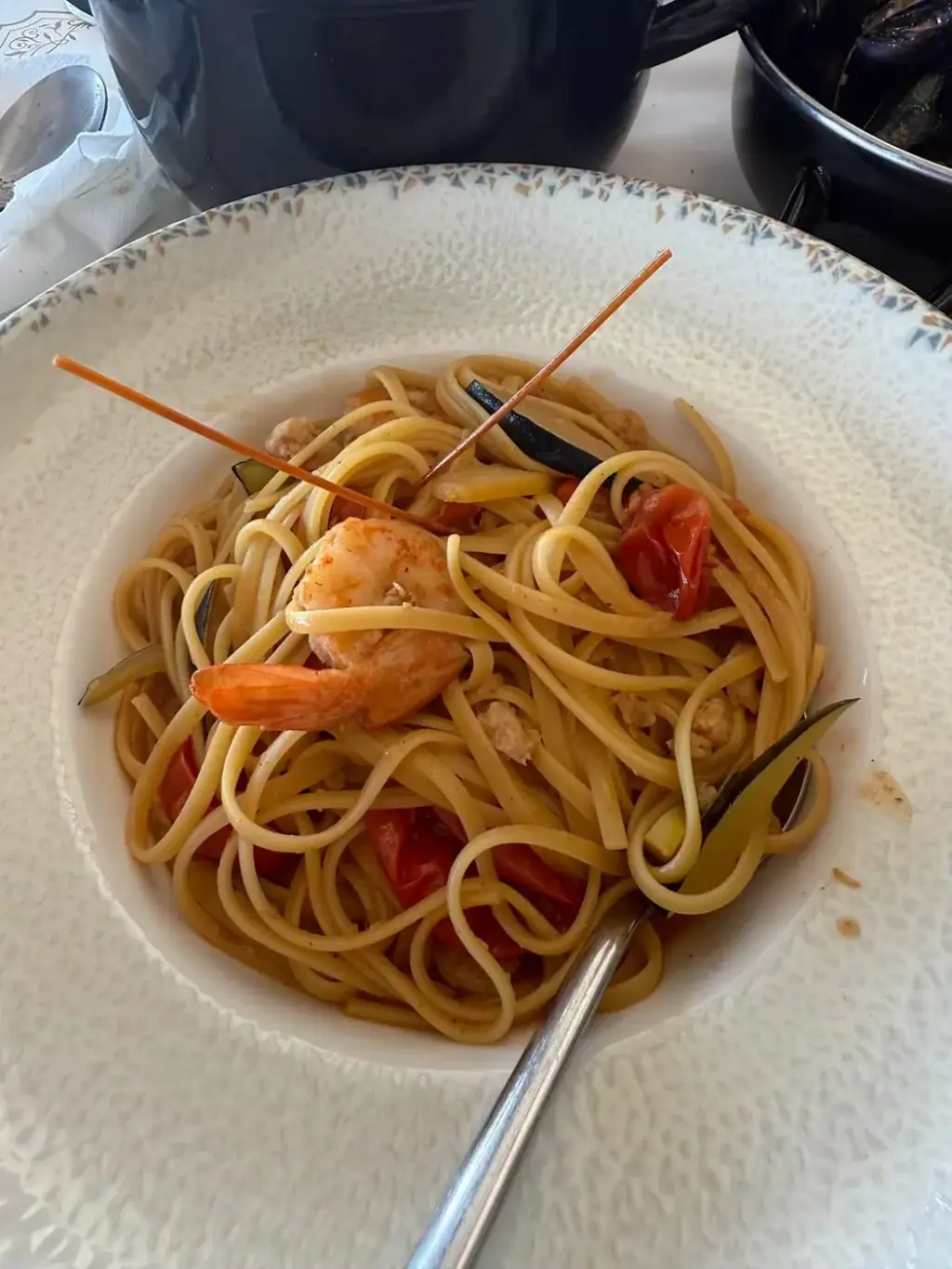 Linguine with a whole prawn, cherry tomatoes and strips of courgette in a white bowl