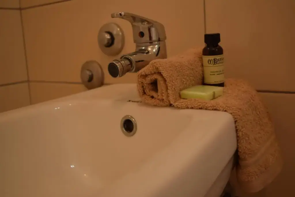 A basin with a folded towel over the edge, a bar of soap and a small bottle of toiletries