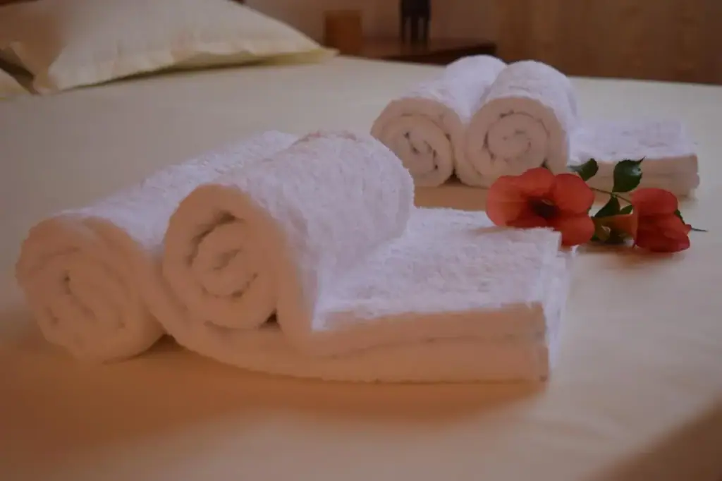 Rolled and folded white towels on a bed with a red hibiscus flower laid beside them