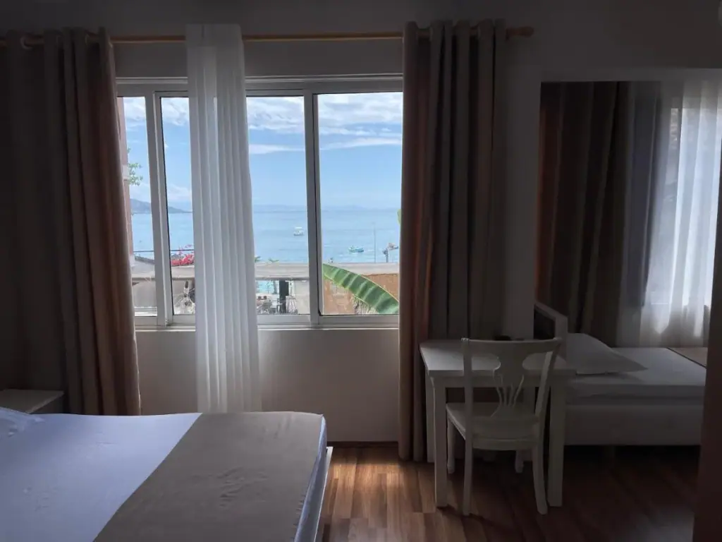 A guest room with a wide window over the bay, a writing desk and chair, wooden floor and a second bed beyond.