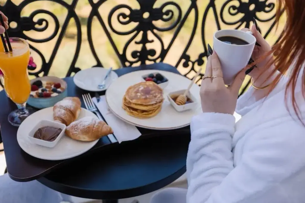 Breakfast on a balcony at Chimaera Hotel: pancakes, croissants, fruit and coffee on a dark table against the scrolled iron rail