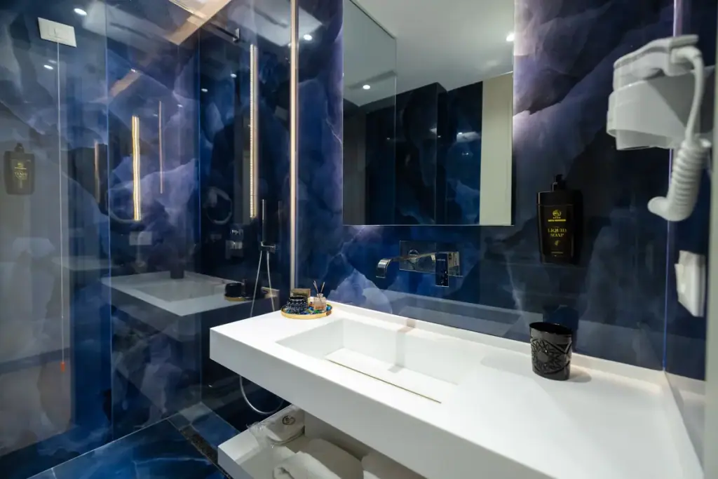 A bathroom at Chimaera Hotel lined in deep blue onyx-patterned tile, with a white stone basin and a walk-in glass shower