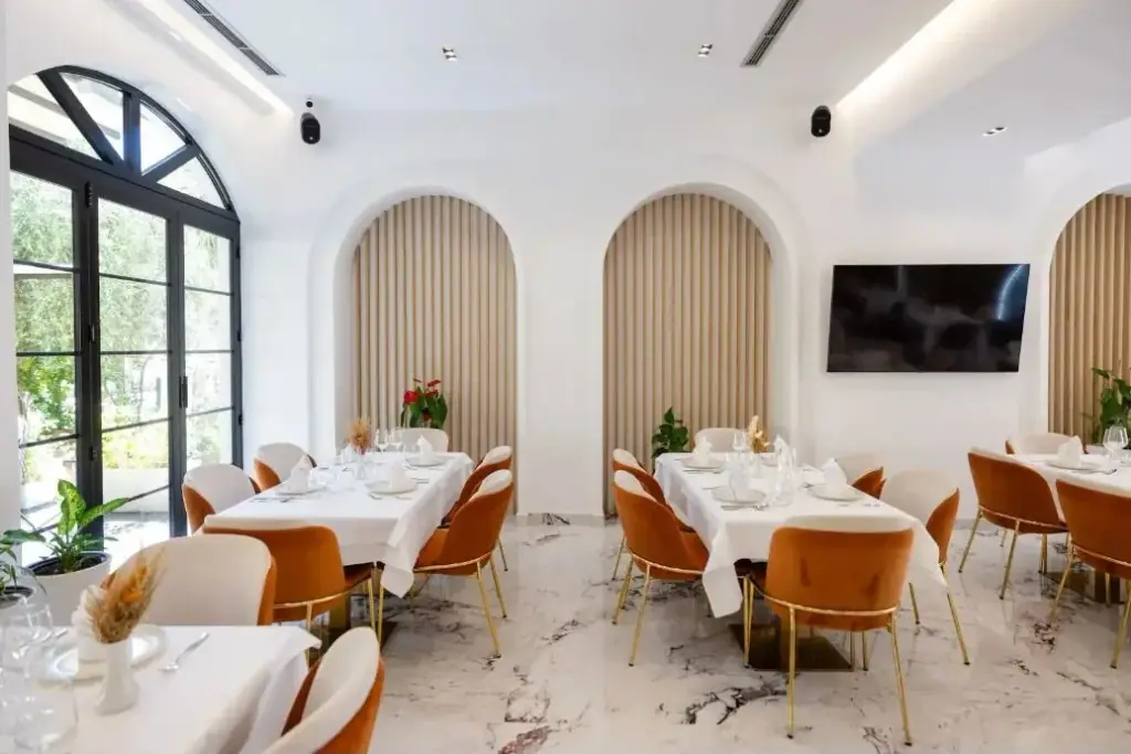 The dining room at Chimaera Hotel, white linen and terracotta velvet chairs on marble, with slatted arched niches along the wall