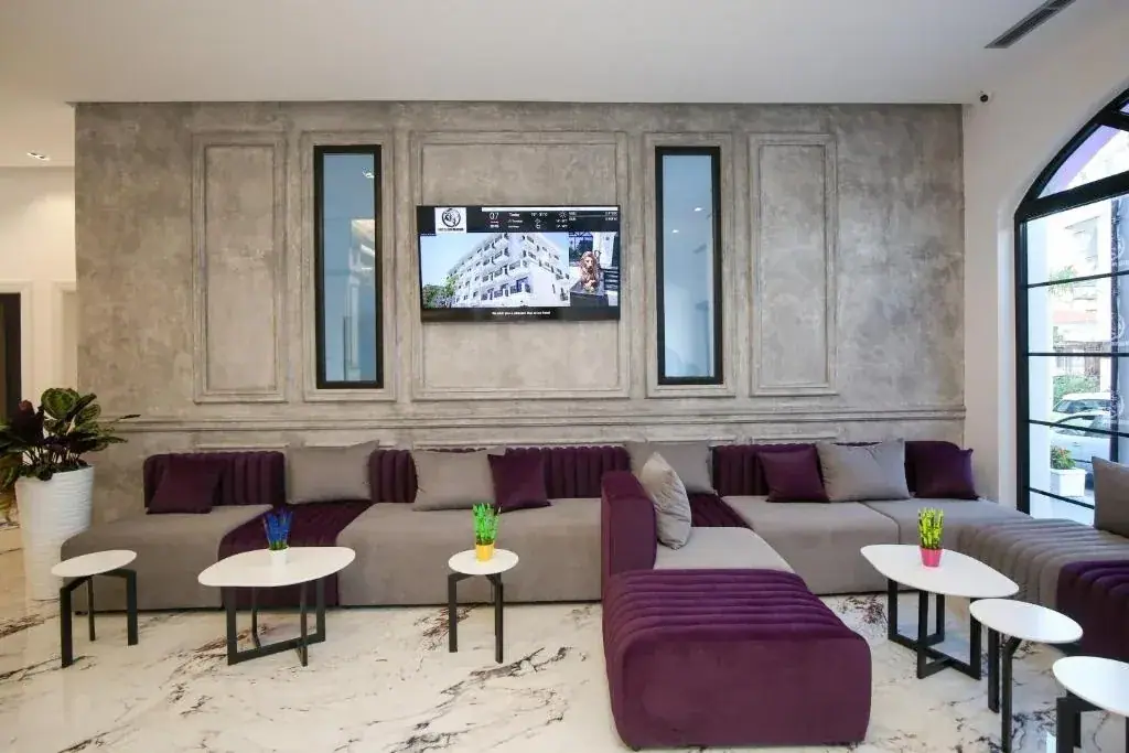 The lobby lounge at Chimaera Hotel with long low seating in grey and plum, small round tables and a panelled plaster wall