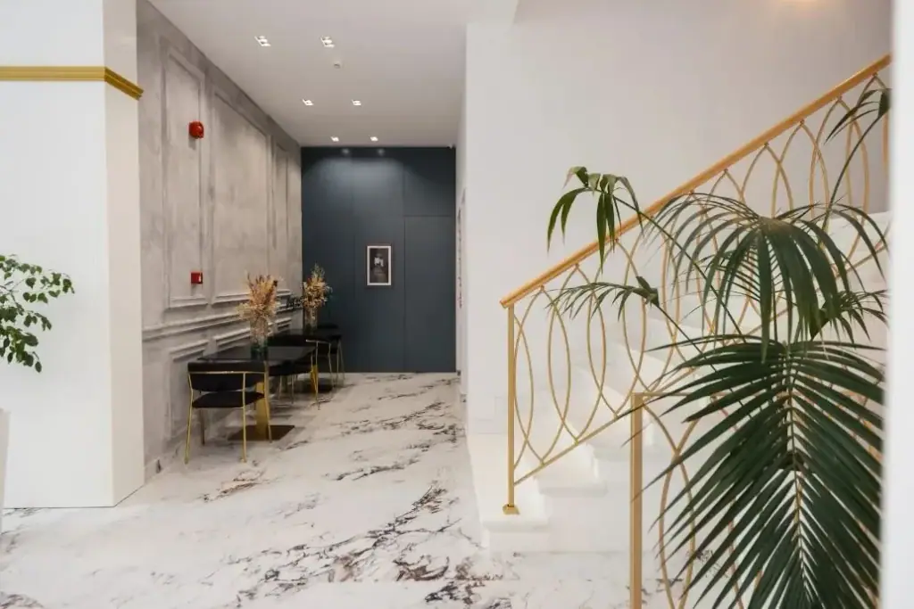 The marble entrance hall at Chimaera Hotel with a brass stair balustrade, a panelled plaster wall and a palm beside the steps