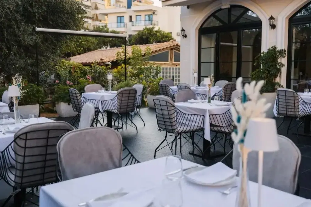 The restaurant terrace at Chimaera Hotel at dusk, laid tables under an awning beside the arched garden doors