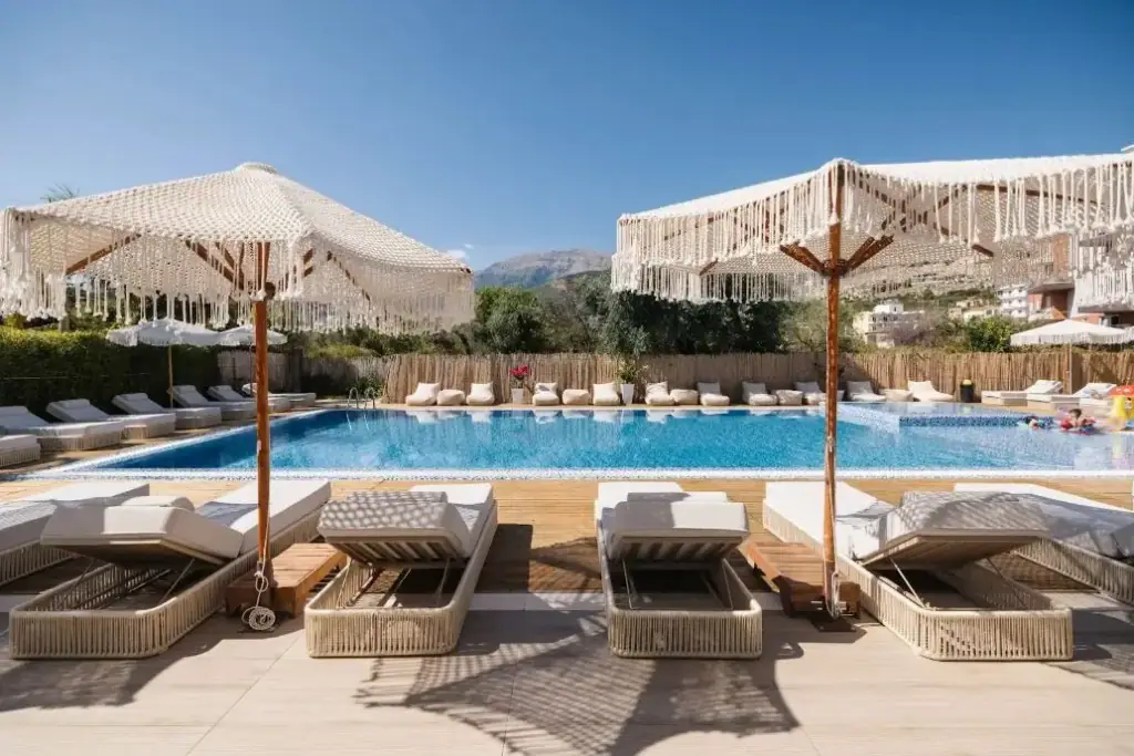Fringed parasols and loungers around the pool at Chimaera Hotel, with the Ceraunian ridge rising behind the trees