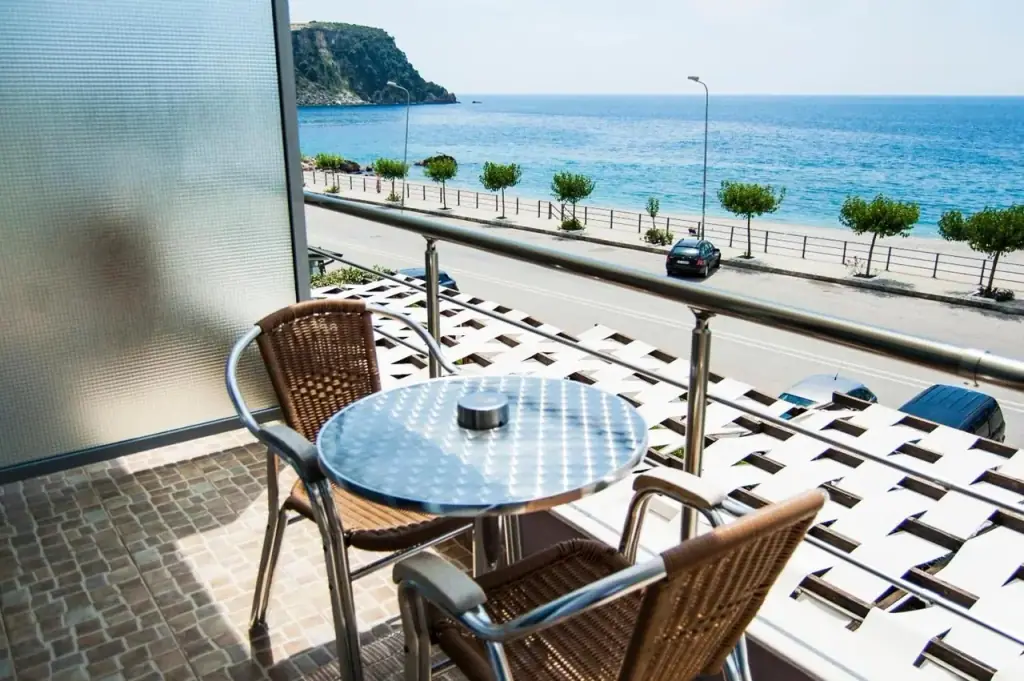 A round balcony table and wicker chairs looking over the coast road to the water