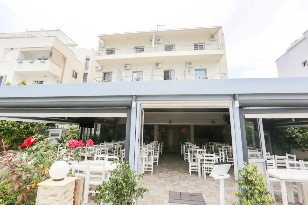White chairs and tables set out under the hotel's canopy in daylight, with the building rising behind