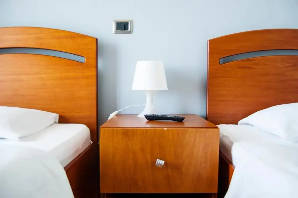 Two single beds either side of a cherry-wood cabinet with a lamp and a remote