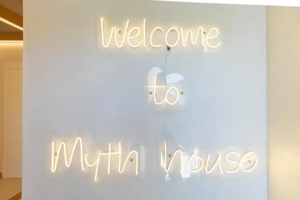 A warm-white neon script on the wall inside Dimitri Hotel reading Welcome to Myth house