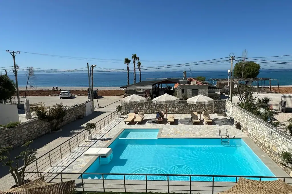 Looking down over the pool at Dimitri Hotel to the shingle of Livadhi Beach and the Ionian a few steps beyond it, past palms and a low stone wall