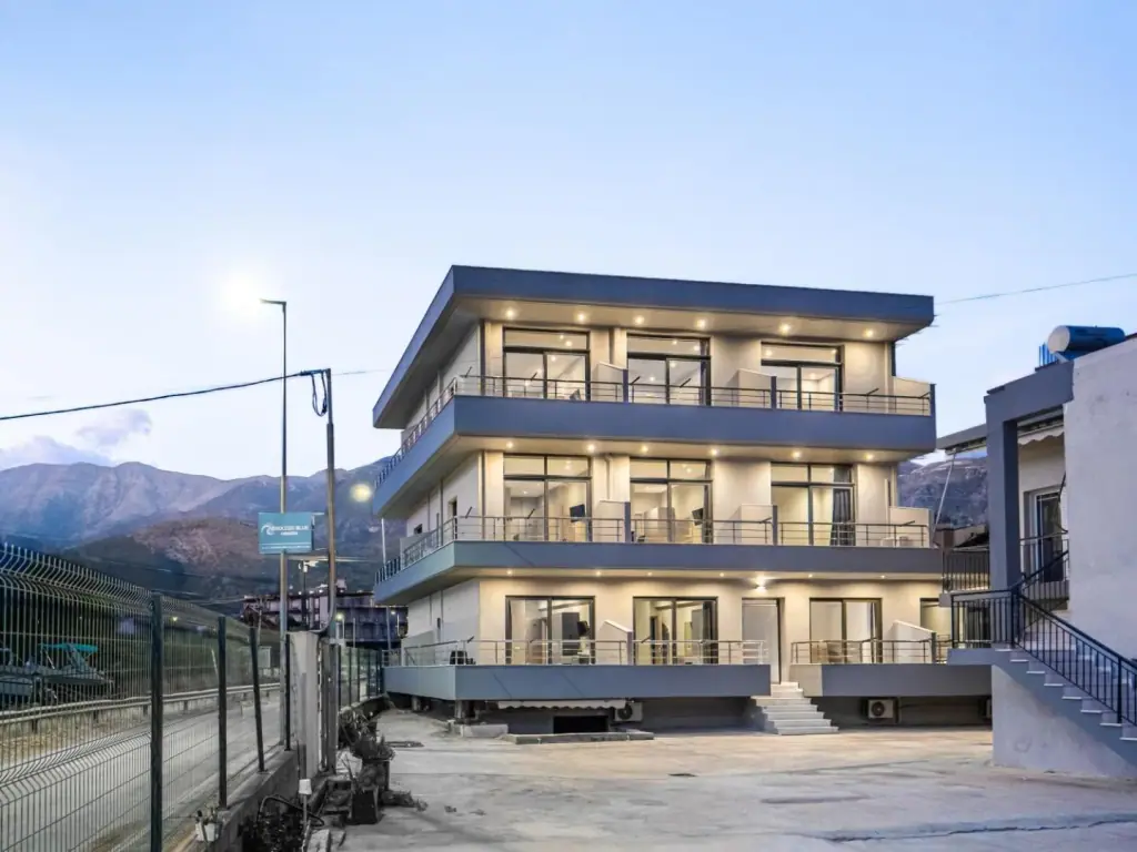 Endless Blue Himara at dusk, three storeys of lit balconies with the mountains behind