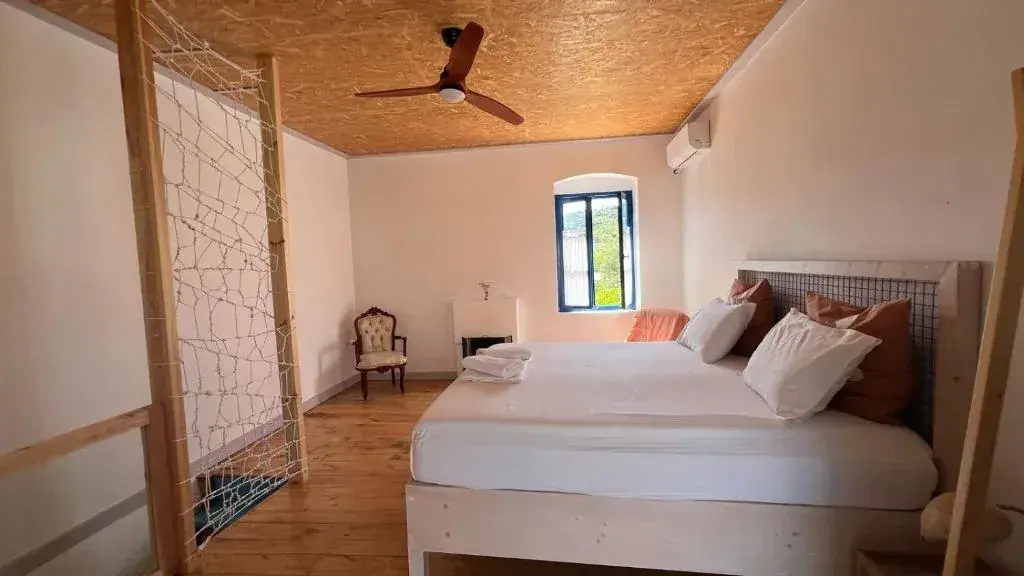 Bedroom of the apartment at Himara Hostel with a king bed, a ceiling fan under a timber ceiling and an arched window
