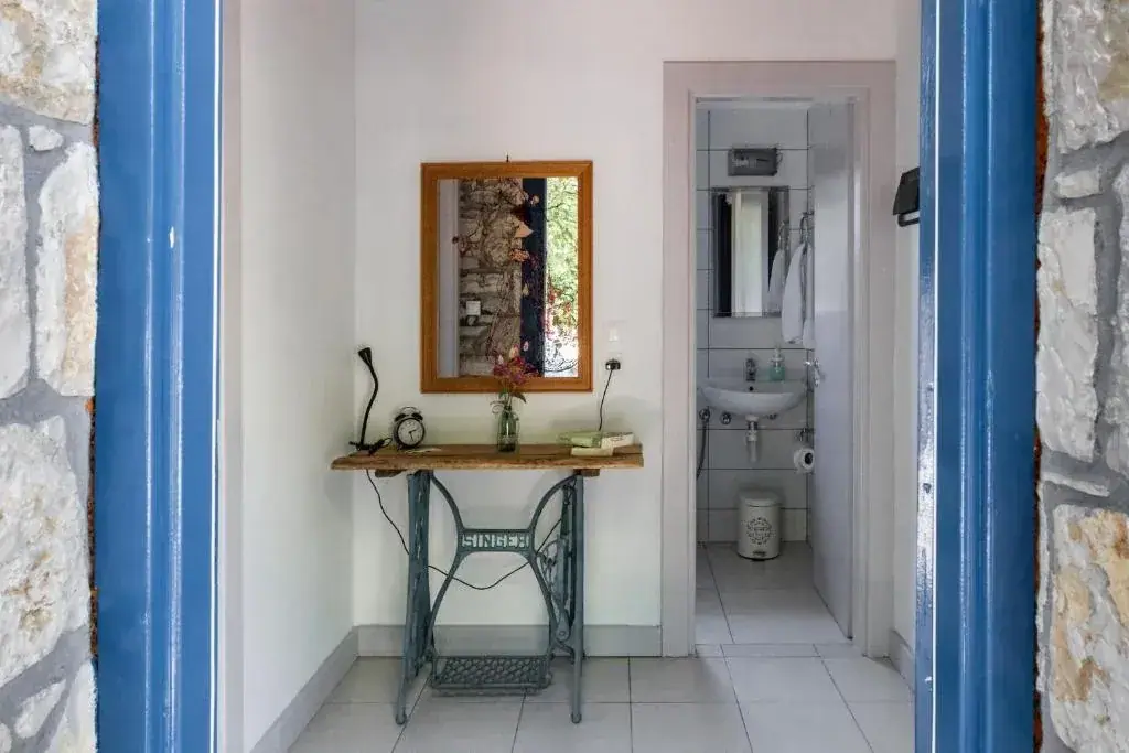 Landing at Himara Hostel seen through a blue-painted stone doorway, with a table built on a Singer sewing-machine base and a shared bathroom beyond