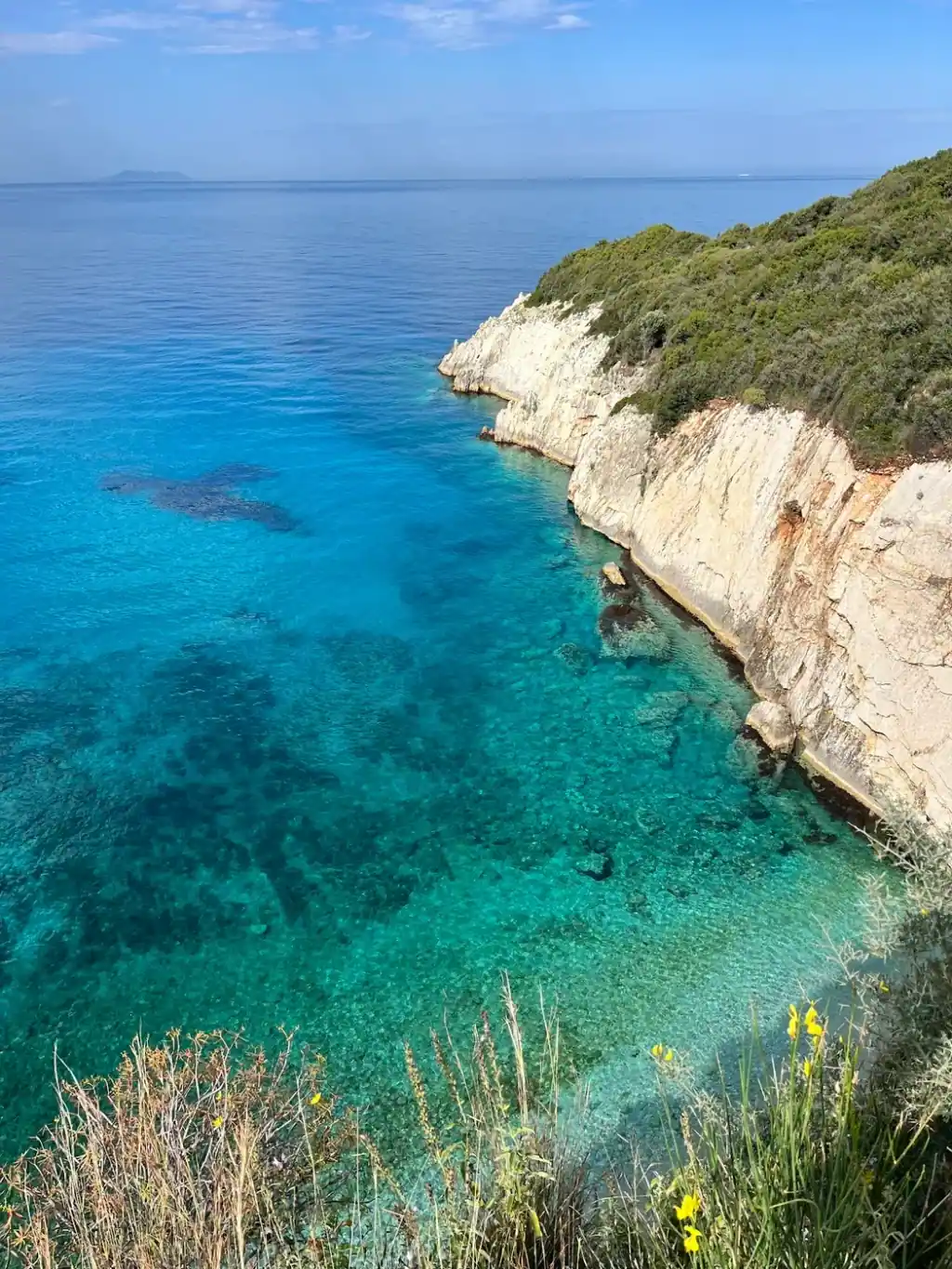 Looking down from a cliff top over turquoise water against a white limestone wall