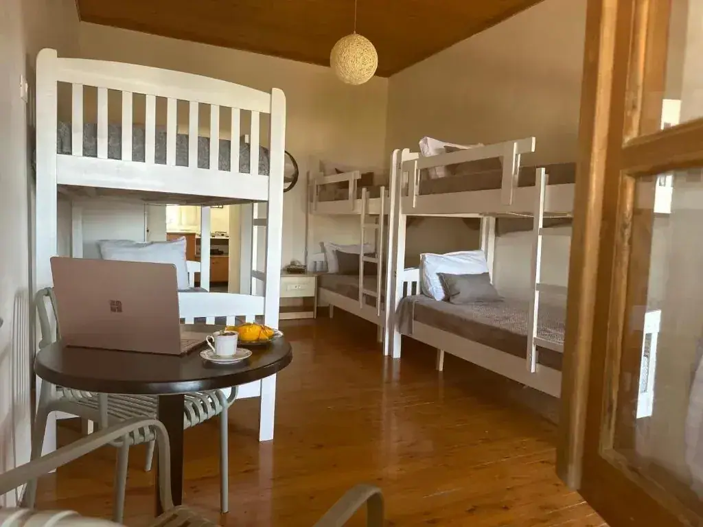 A dormitory corner with a round dark table and two chairs beside the bunk beds, a coffee cup and a plate of sliced fruit on the table