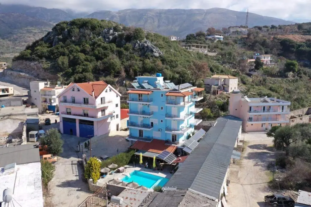 Hotel Frida from above: a five-storey building with balconies on the hillside at Himarë, its swimming pool and terrace on the level below